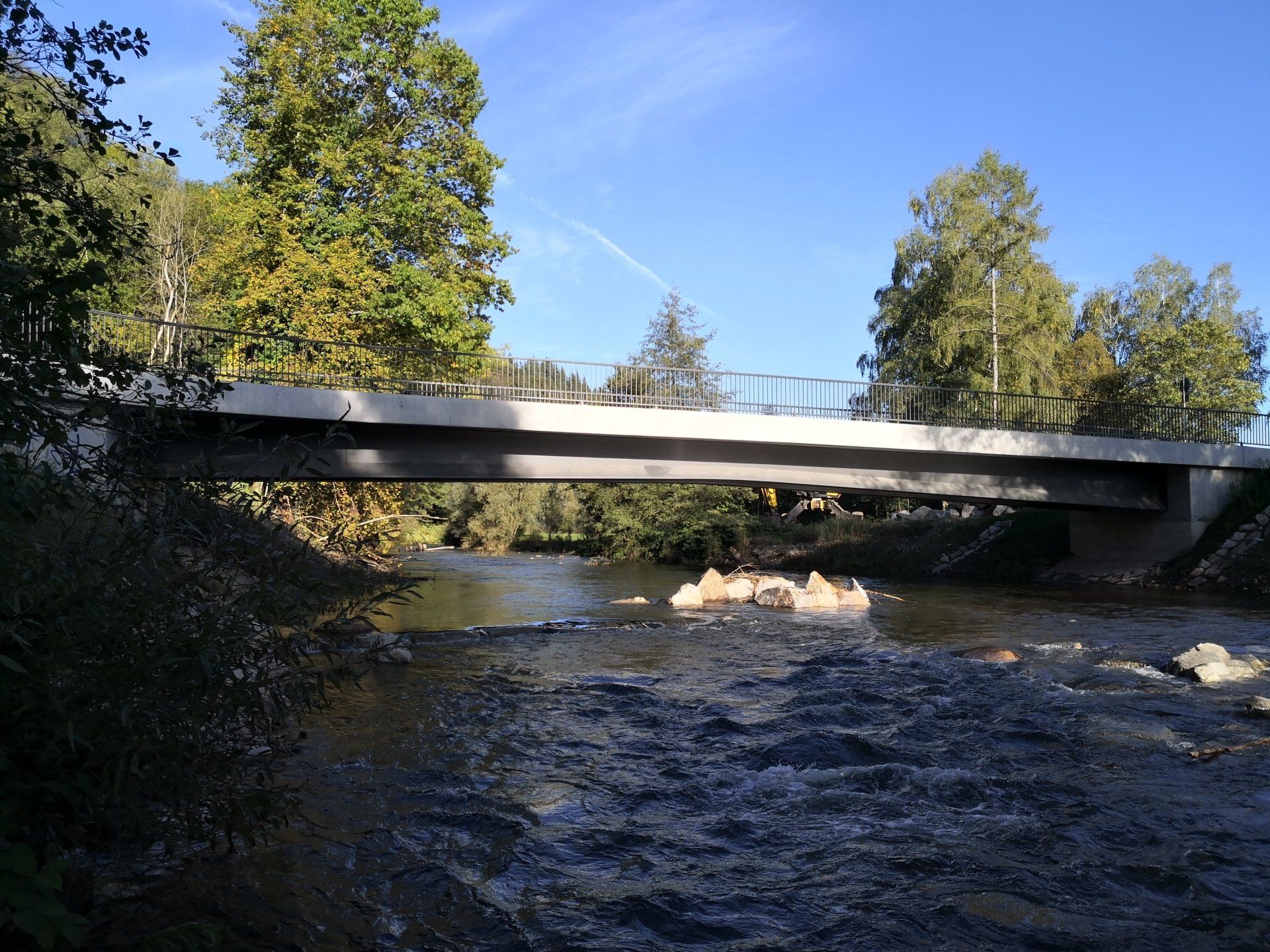 Ein Fluss fließt unter einer niedrigen Betonbrücke hindurch, eingerahmt von Bäumen und blauem Himmel