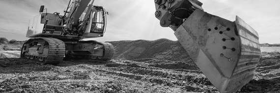 Ein Bagger ist auf einer schlammigen Baustelle im Einsatz und hebt im Vordergrund eine große Schaufel an.