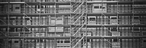 Graue Gerüste und Metallträger verdecken die Fassade eines im Bau befindlichen Gebäudes.