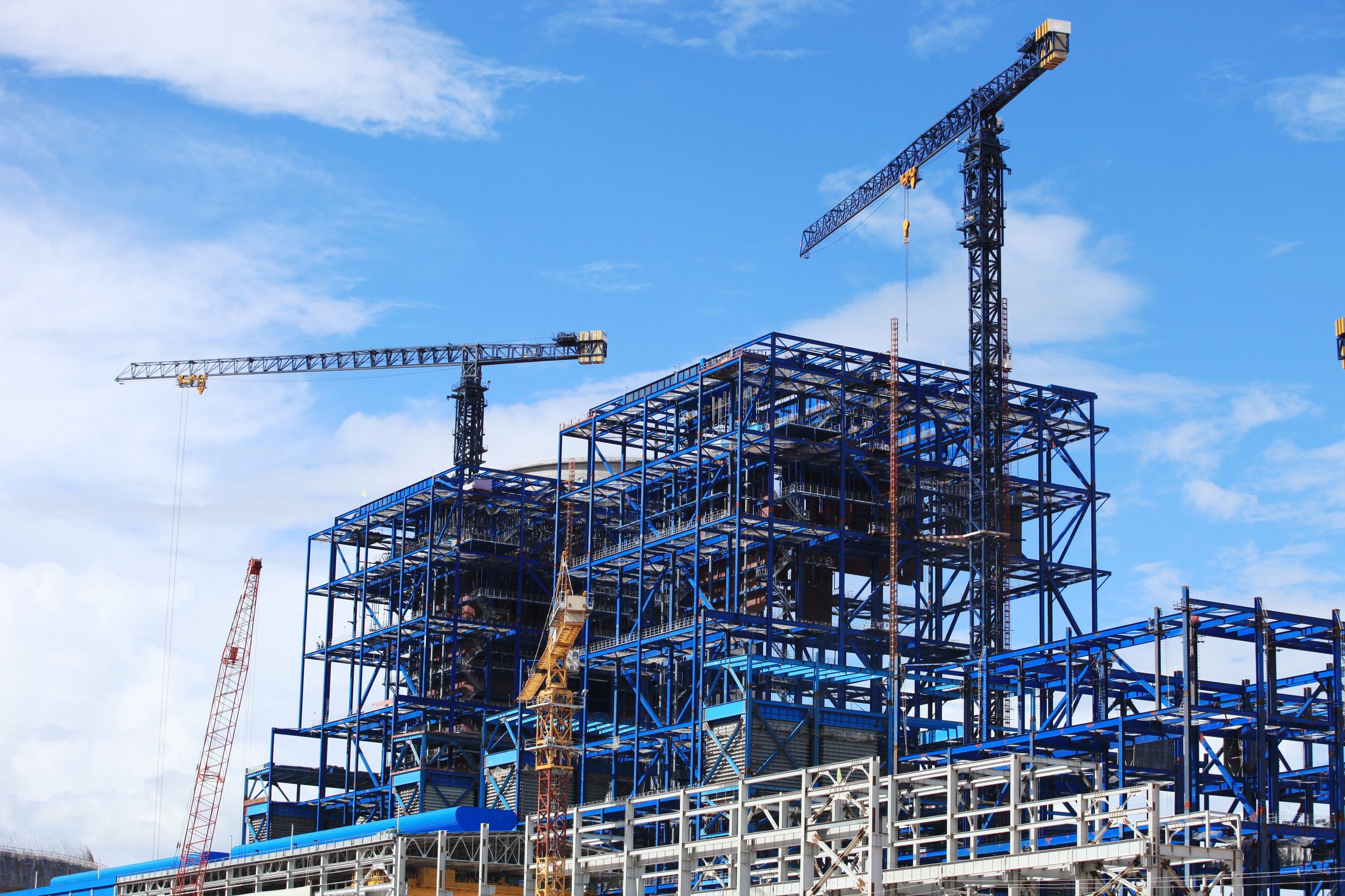 Baustelle mit Stahlgerüst und Kränen vor blauem Himmel