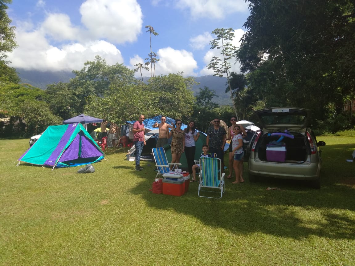 Um grupo de pessoas está em volta de uma tenda em um campo.
