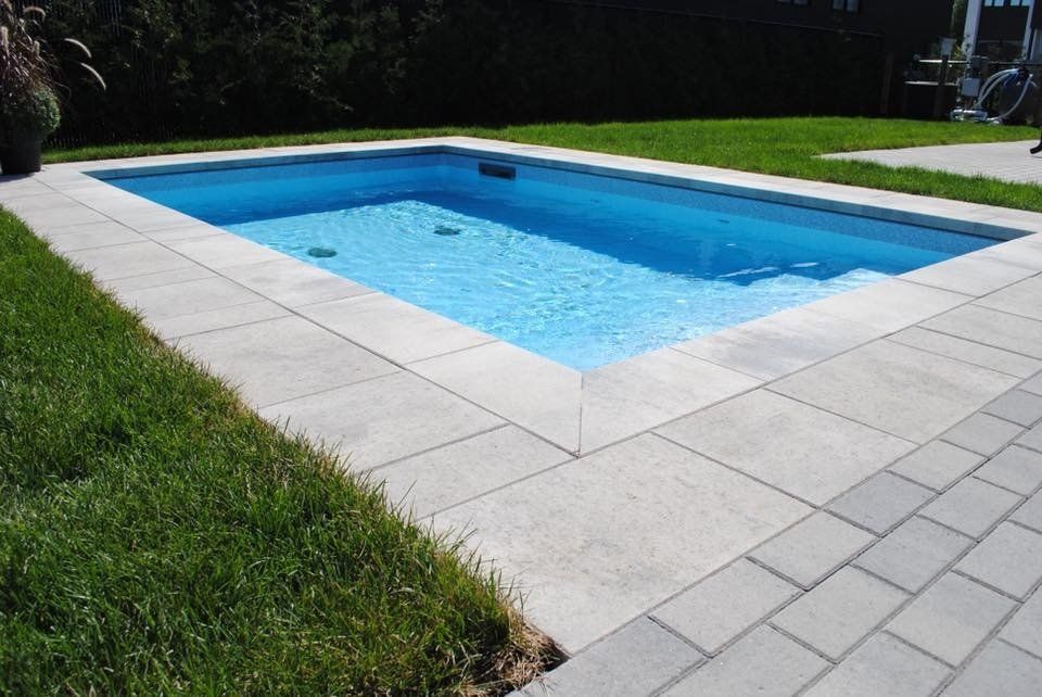 Une grande piscine rectangulaire entourée d'herbe et de briques