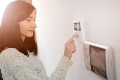 Woman enters code on a white security system keypad on a white wall.