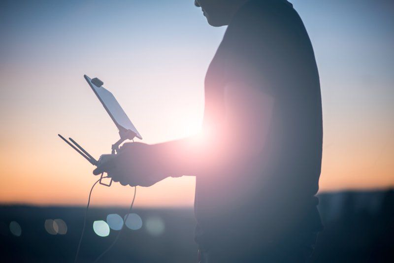 A man is holding a remote control in front of a sunset.
