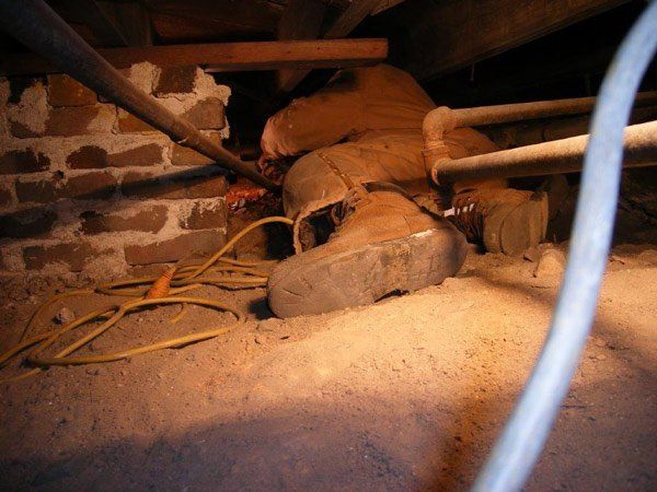 A pair of boots is laying on the ground in an attic.