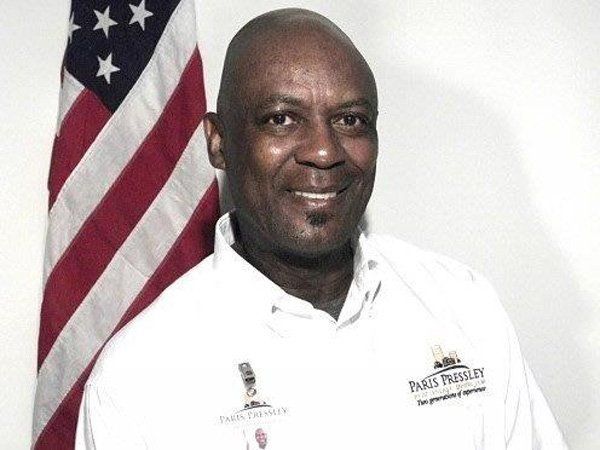 A man wearing a white shirt that says parks and recreation stands in front of an american flag