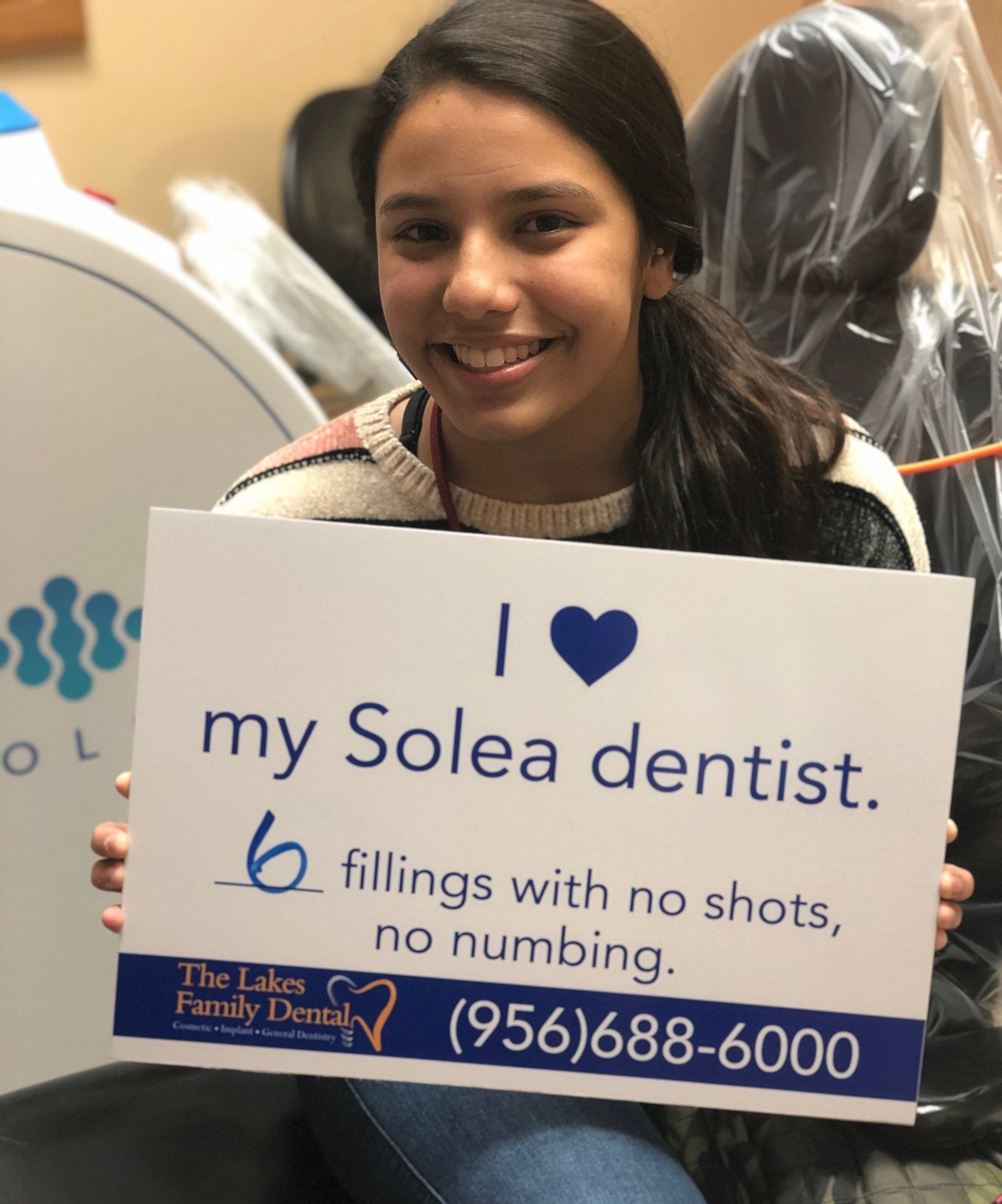 A girl holding a sign that says i love my solea dentist