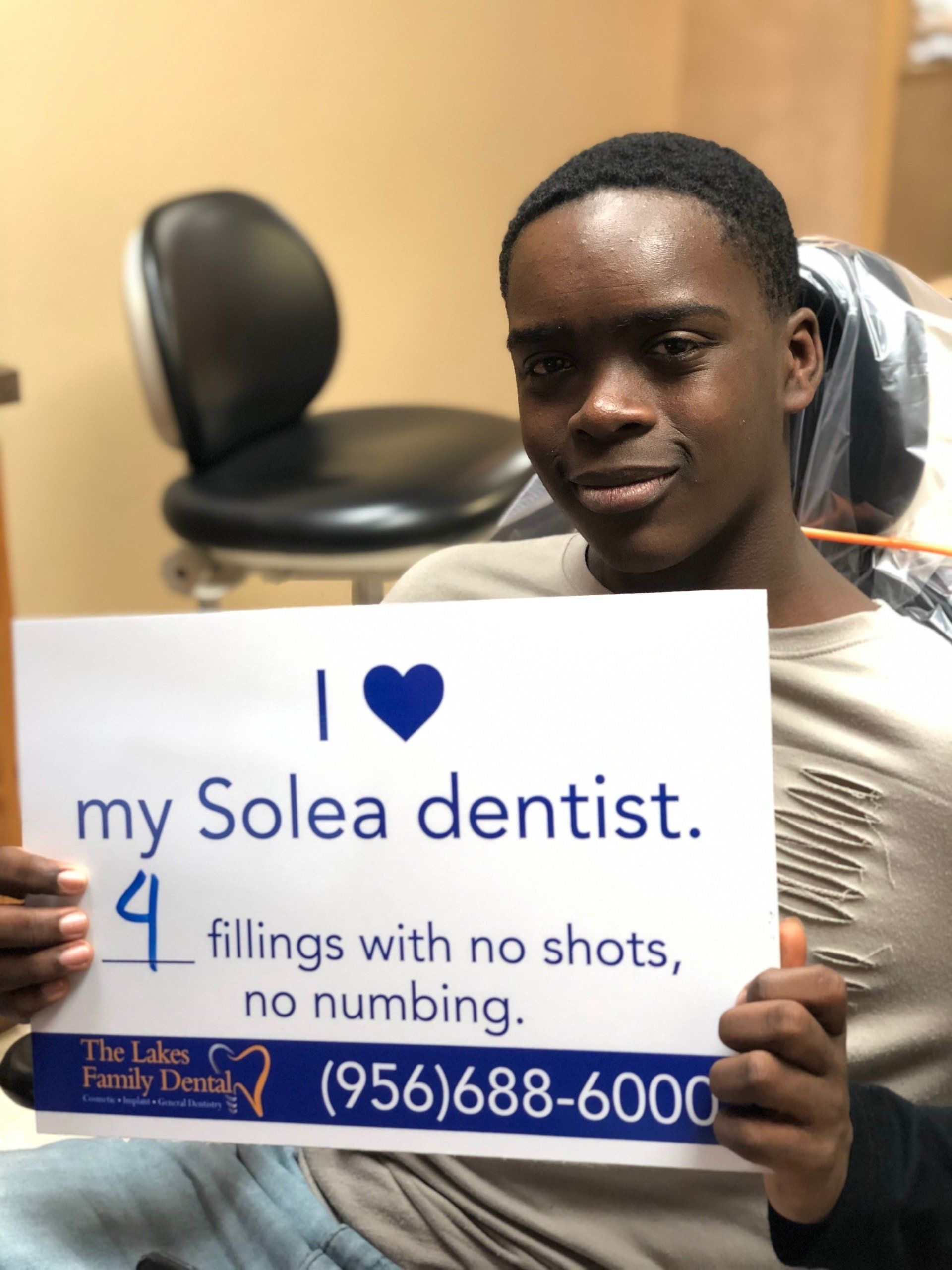 A young man holding a sign that says i love my solea dentist