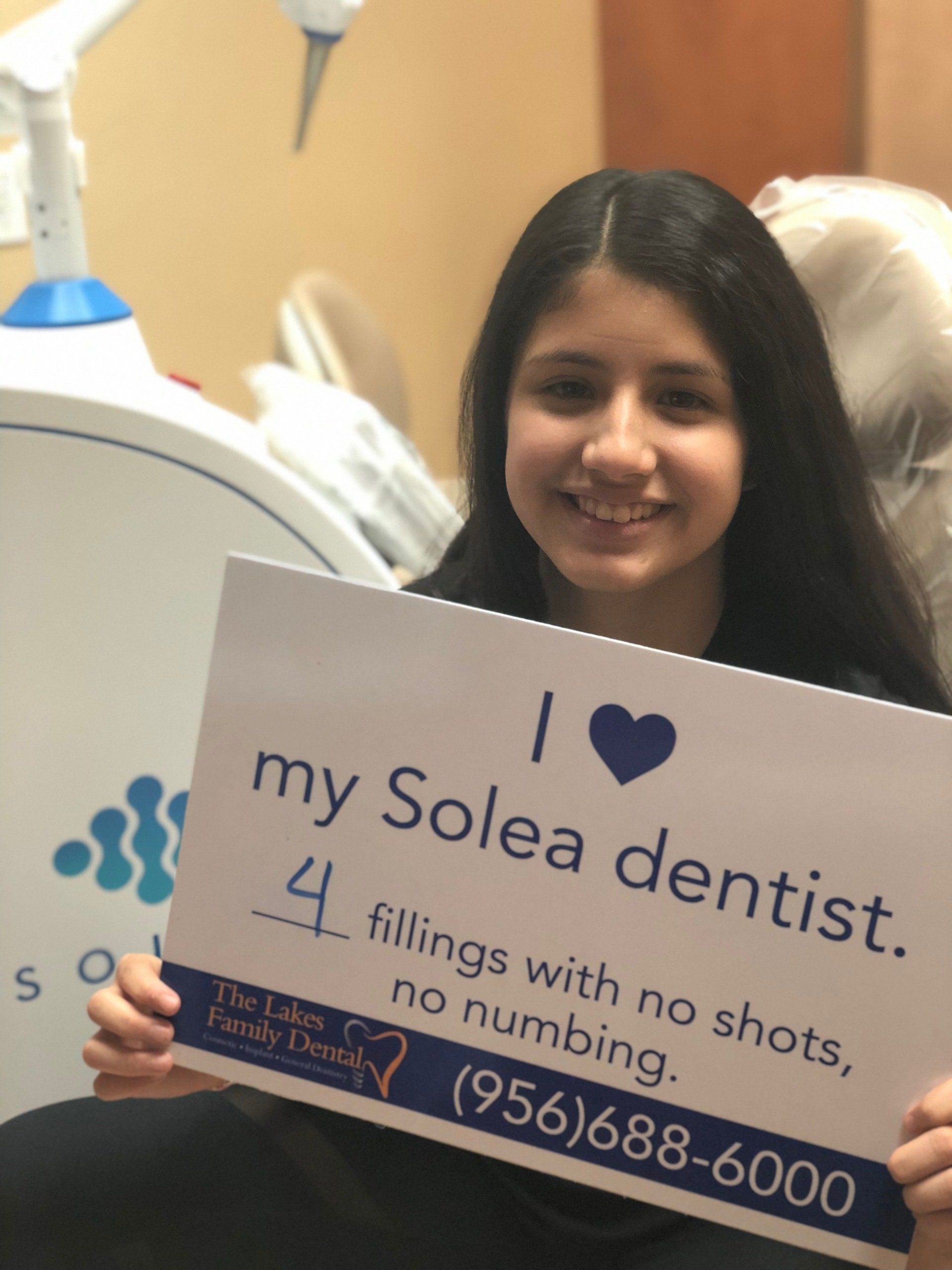 A girl holding a sign that says i love my solea dentist