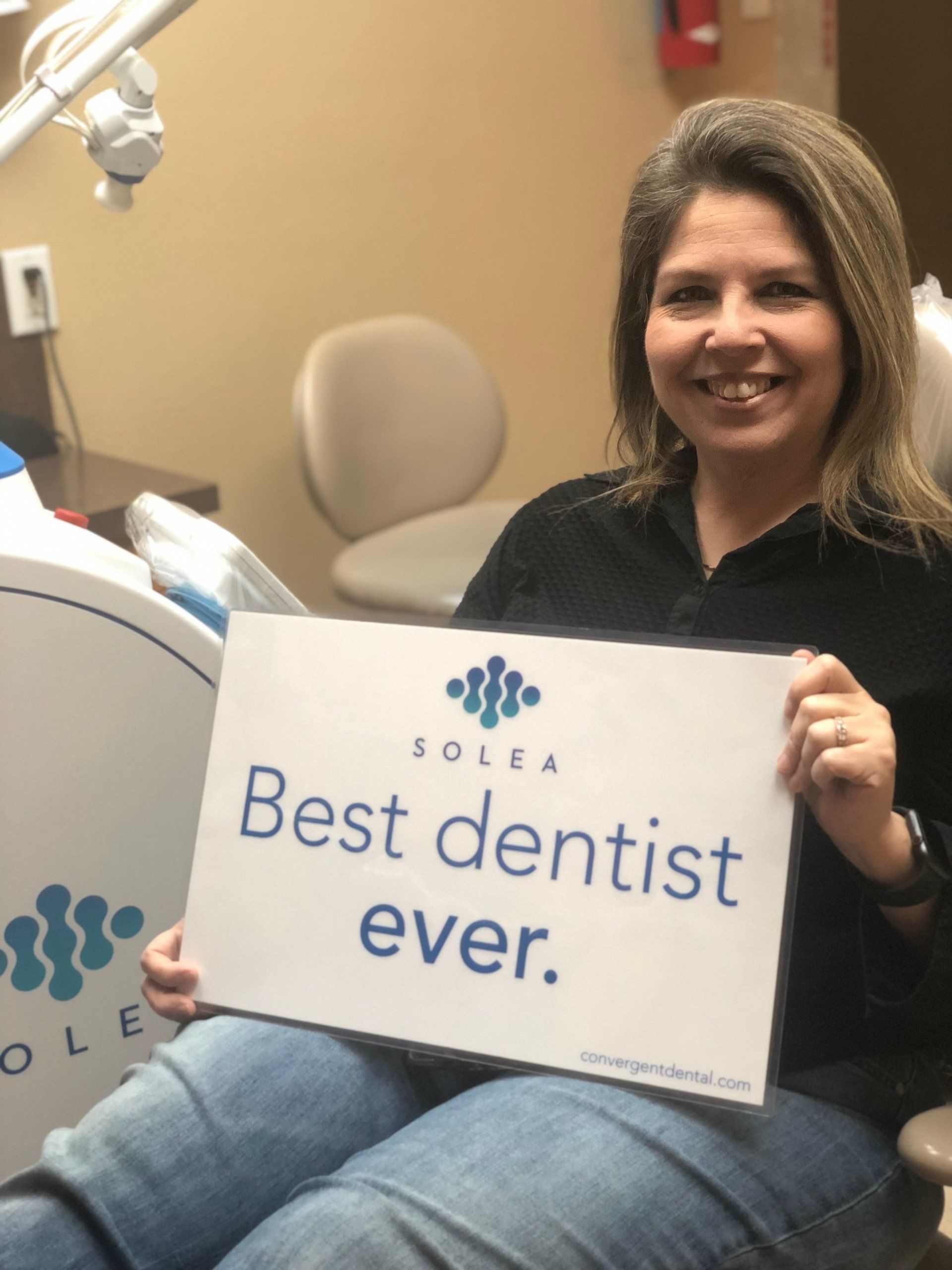 A woman in a dental chair holding a sign that says best dentist ever