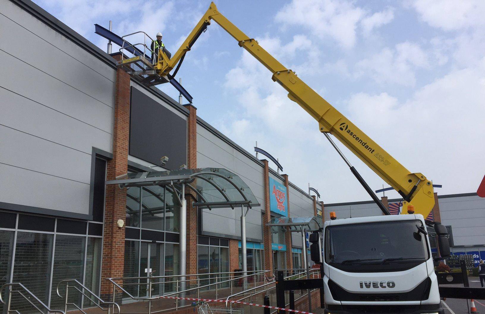Cherry picker accessing roof on tall retail building