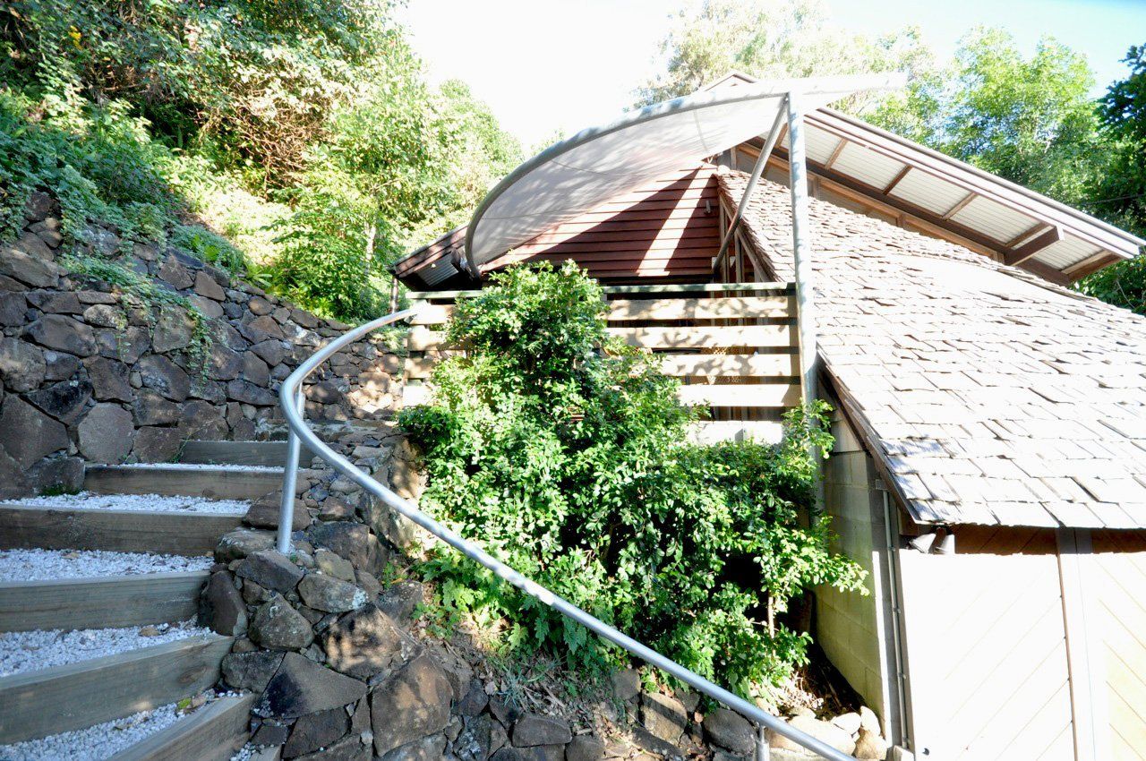 Stone steps and a curved metal railing beside a wooden shed on a sunlit hillside