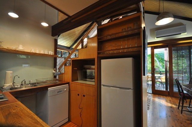 Compact kitchen with wooden cabinets, stainless sink and dishwasher, and a fridge under a lofted wooden ceiling.