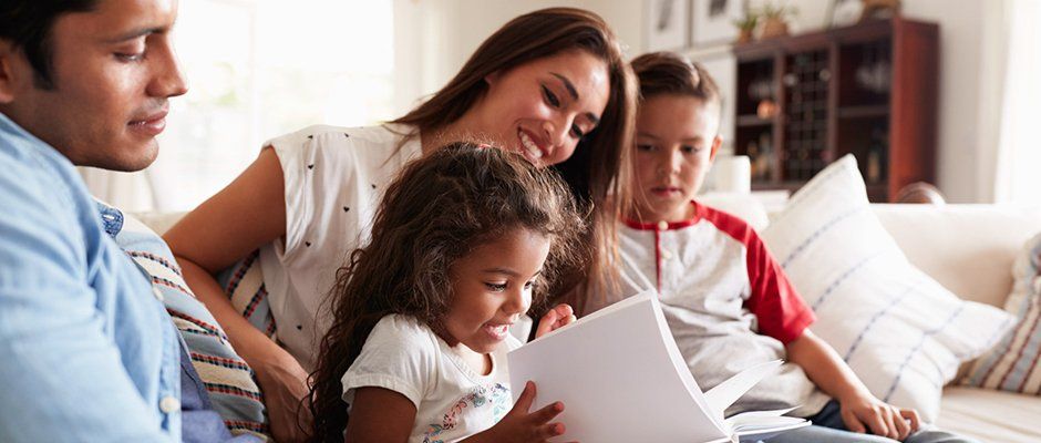 Family of four reading a book on a couch | Bablot