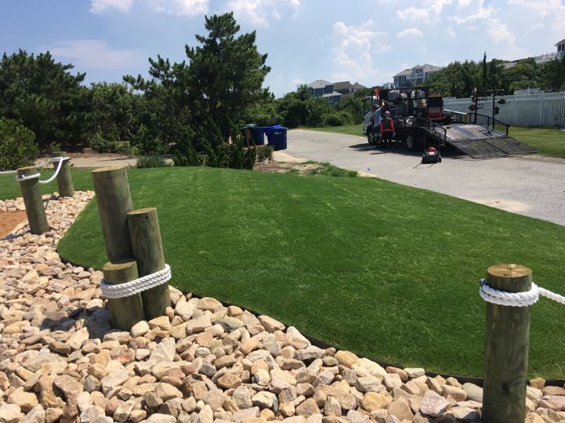 Cobblestone river rock borders a manicured lawn and has a post and rope fence.