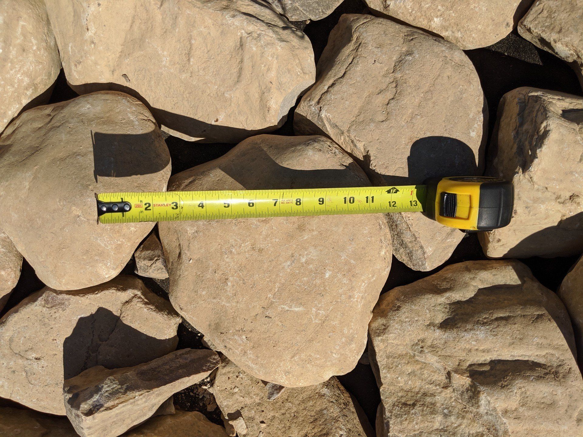 Large river rock with a tape measure showing they are at least 9 inches wide.