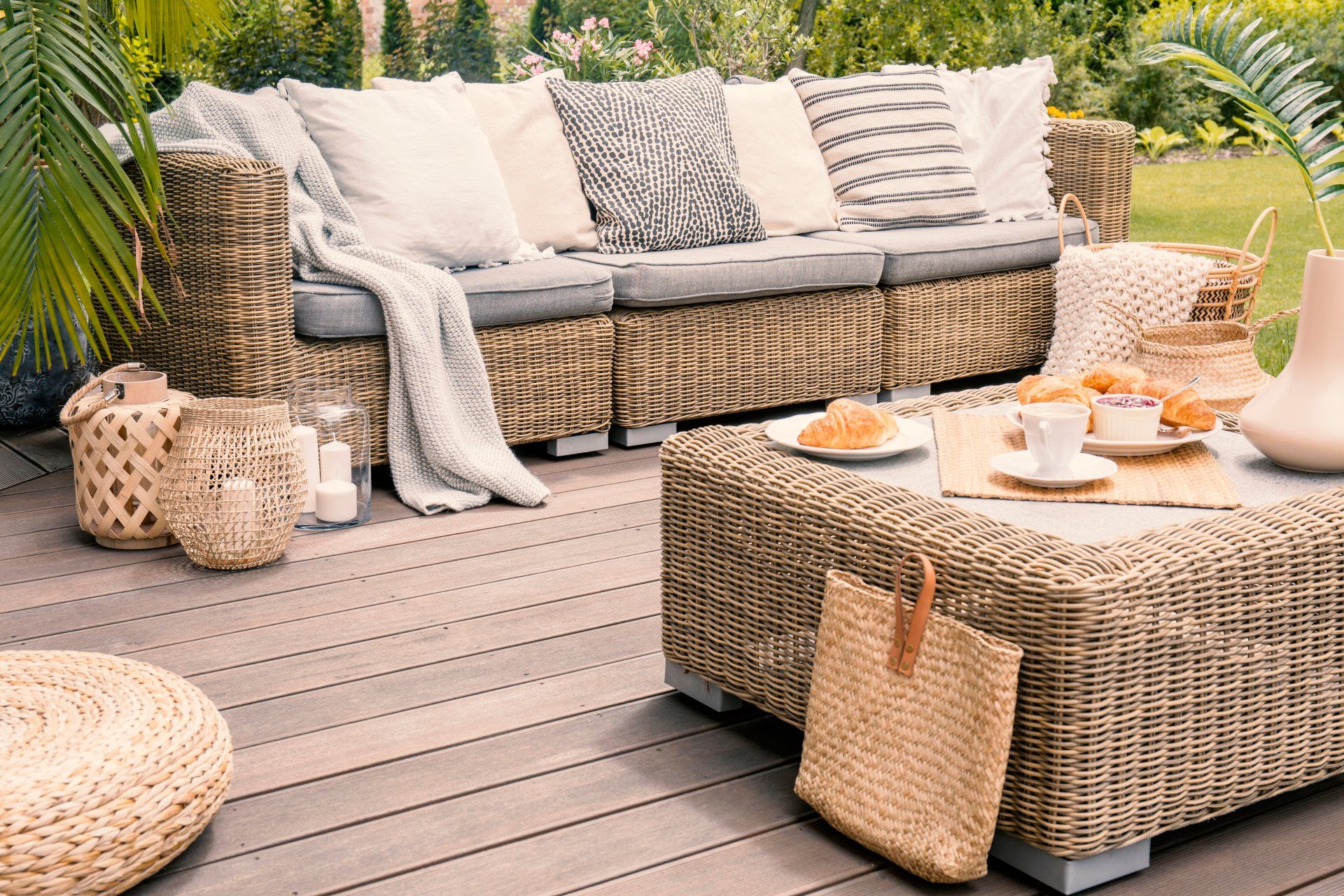 Wicker patio set with beige cushions standing on a wooden board deck. Breakfast on a table on a backyard porch.