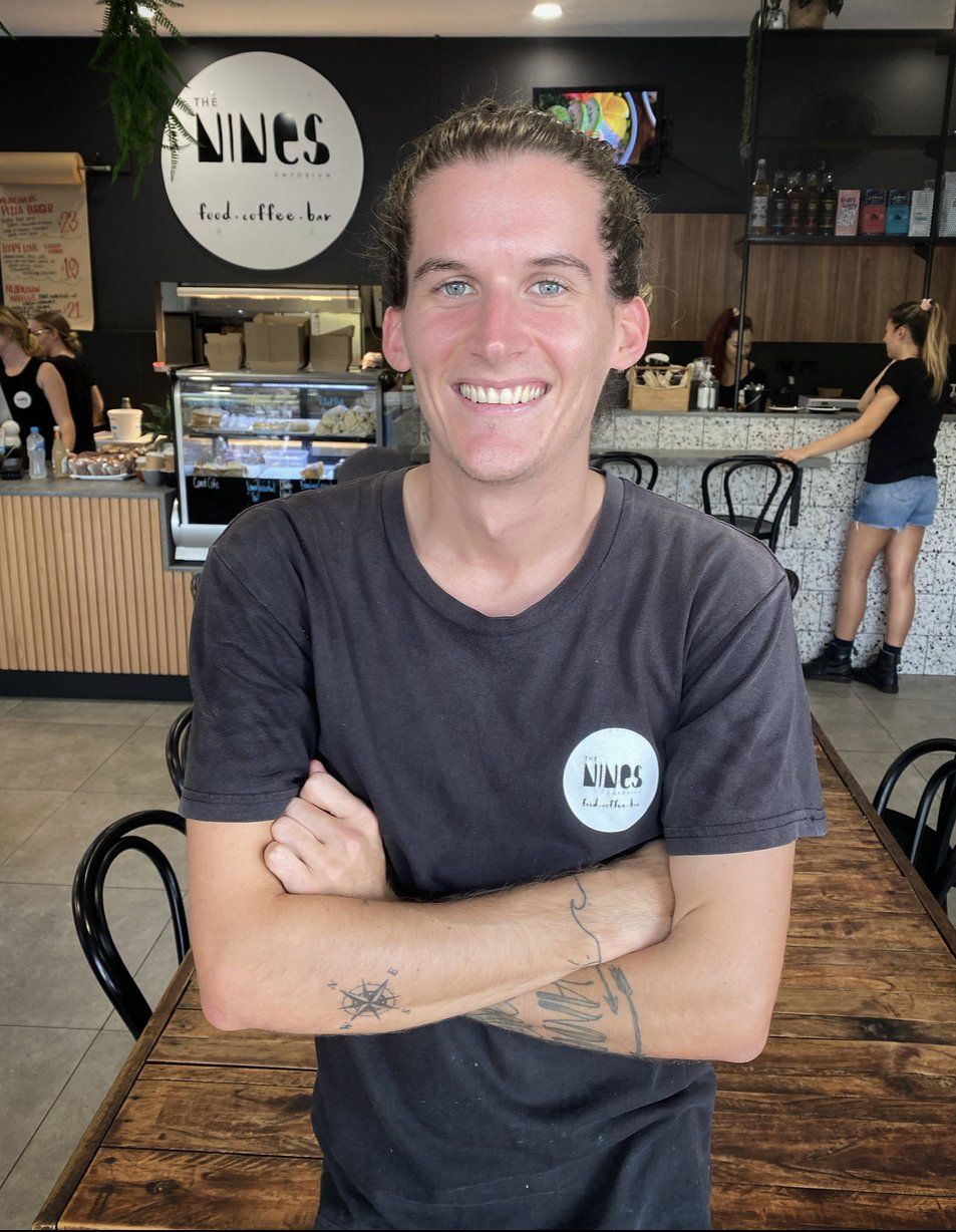 A man in a black shirt is standing with his arms crossed in a restaurant.