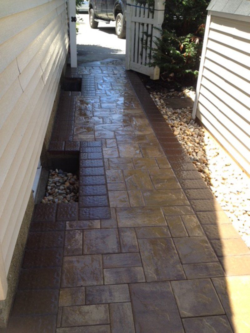 brown stone walkway on the side of house with basement window water drain pits