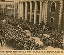 A black and white photo of a funeral procession in front of a large building.