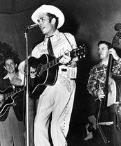 A man in a cowboy hat is singing into a microphone while playing a guitar.