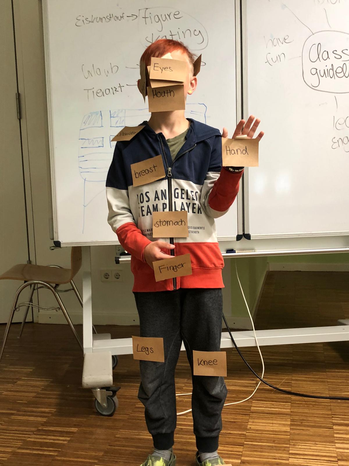 Ein kleiner Junge steht mit Karten im Gesicht vor einem Whiteboard.