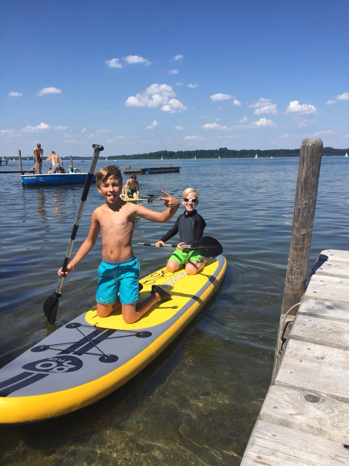 Zwei kleine Jungen knien auf einem Paddelbrett im Wasser.