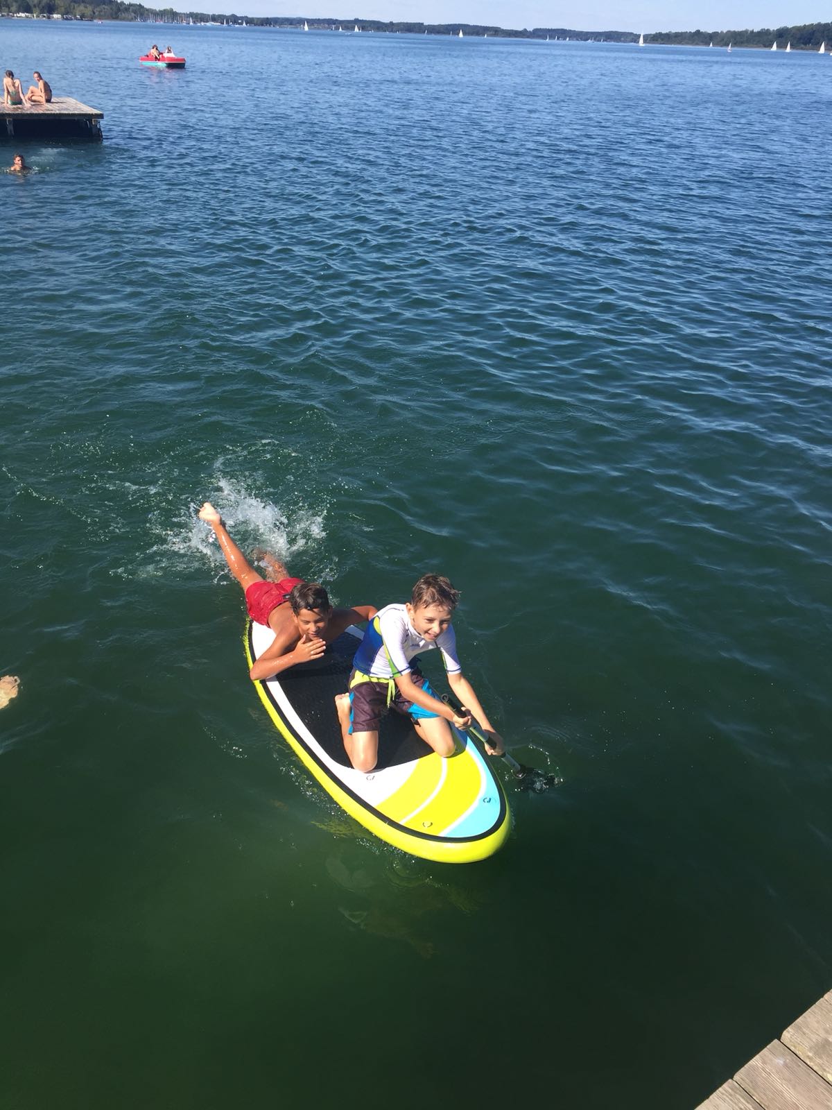 Zwei Kinder fahren auf einem Paddelbrett im Wasser.