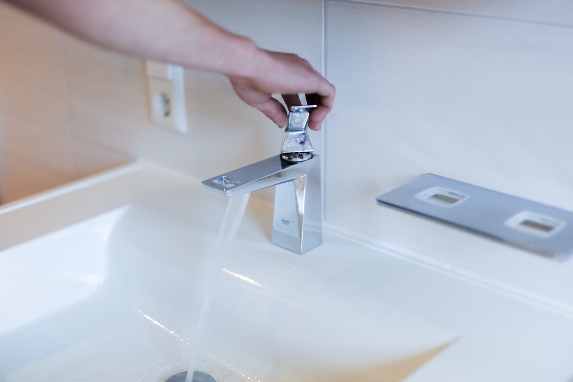 Eine Person dreht den Wasserhahn eines Badezimmerwaschbeckens auf.