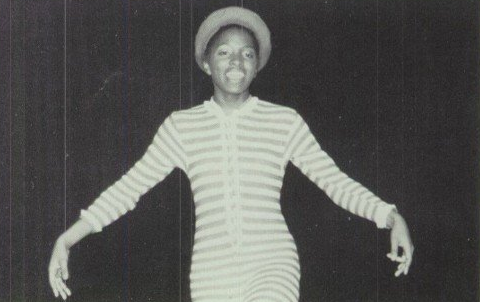 A black and white photo of a girl wearing a striped shirt and hat