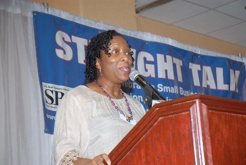 A woman stands at a podium speaking into a microphone in front of a sign that says straight talk