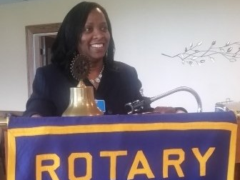 A woman stands behind a podium with a banner that says rotary