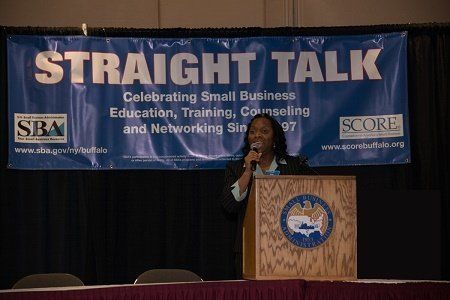 A woman stands at a podium in front of a sign that says straight talk