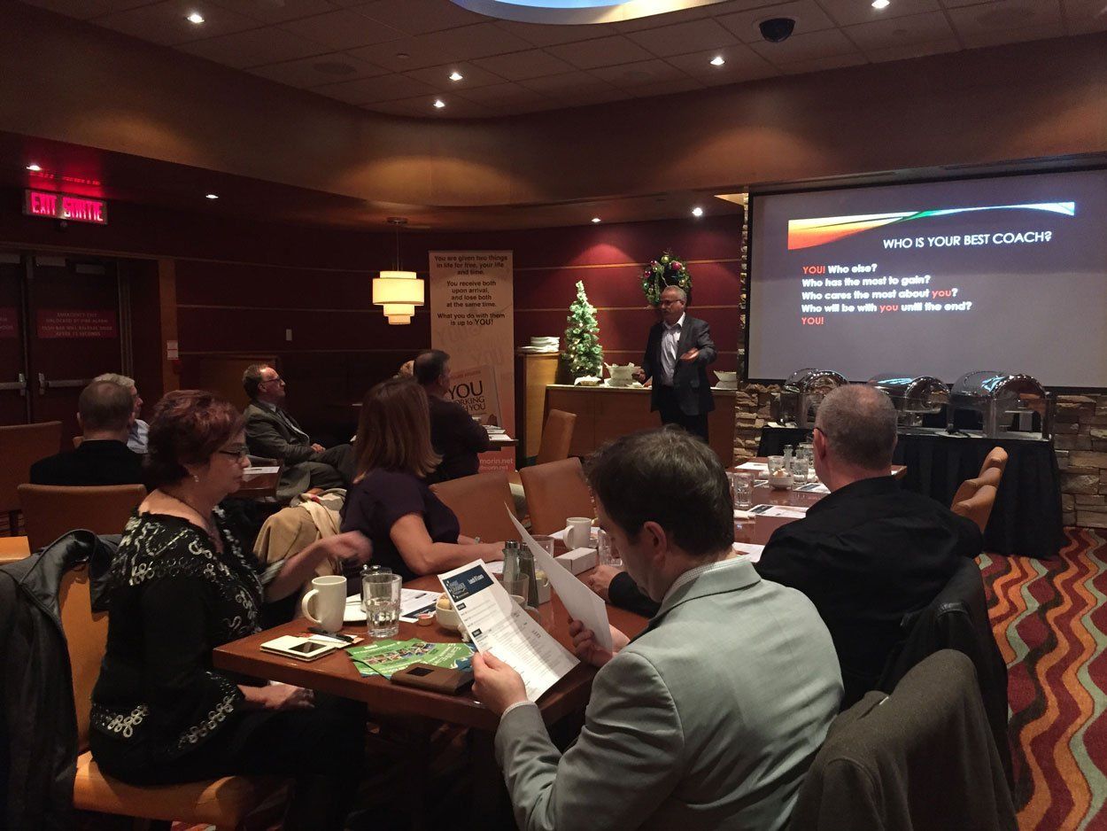 A man giving a presentation in a restaurant, with attendees looking at him and handouts.