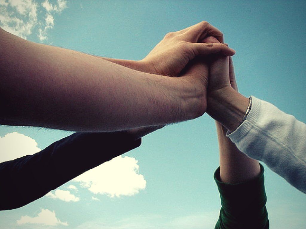 Hands clasped together, reaching towards a blue sky with clouds. Symbol of unity and collaboration.
