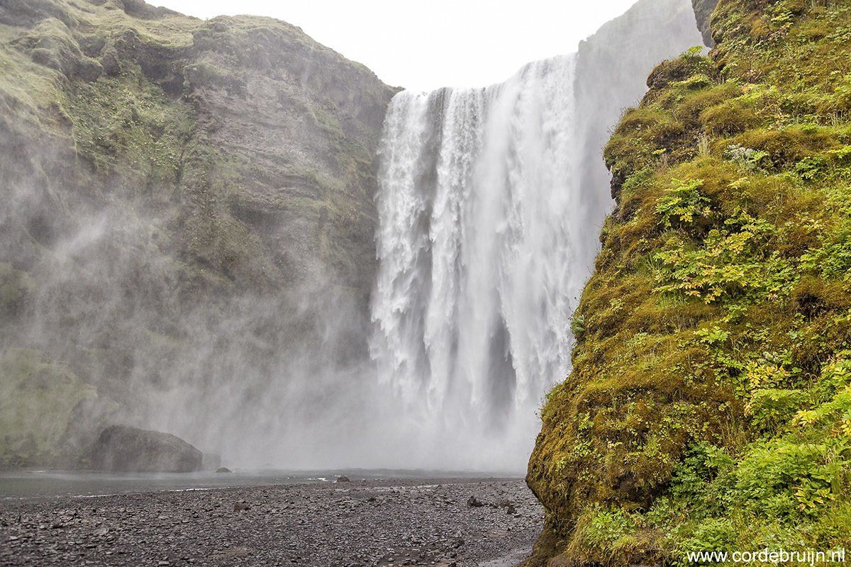 Waterfall cascading down a cliff face, mist rising, rocky foreground.