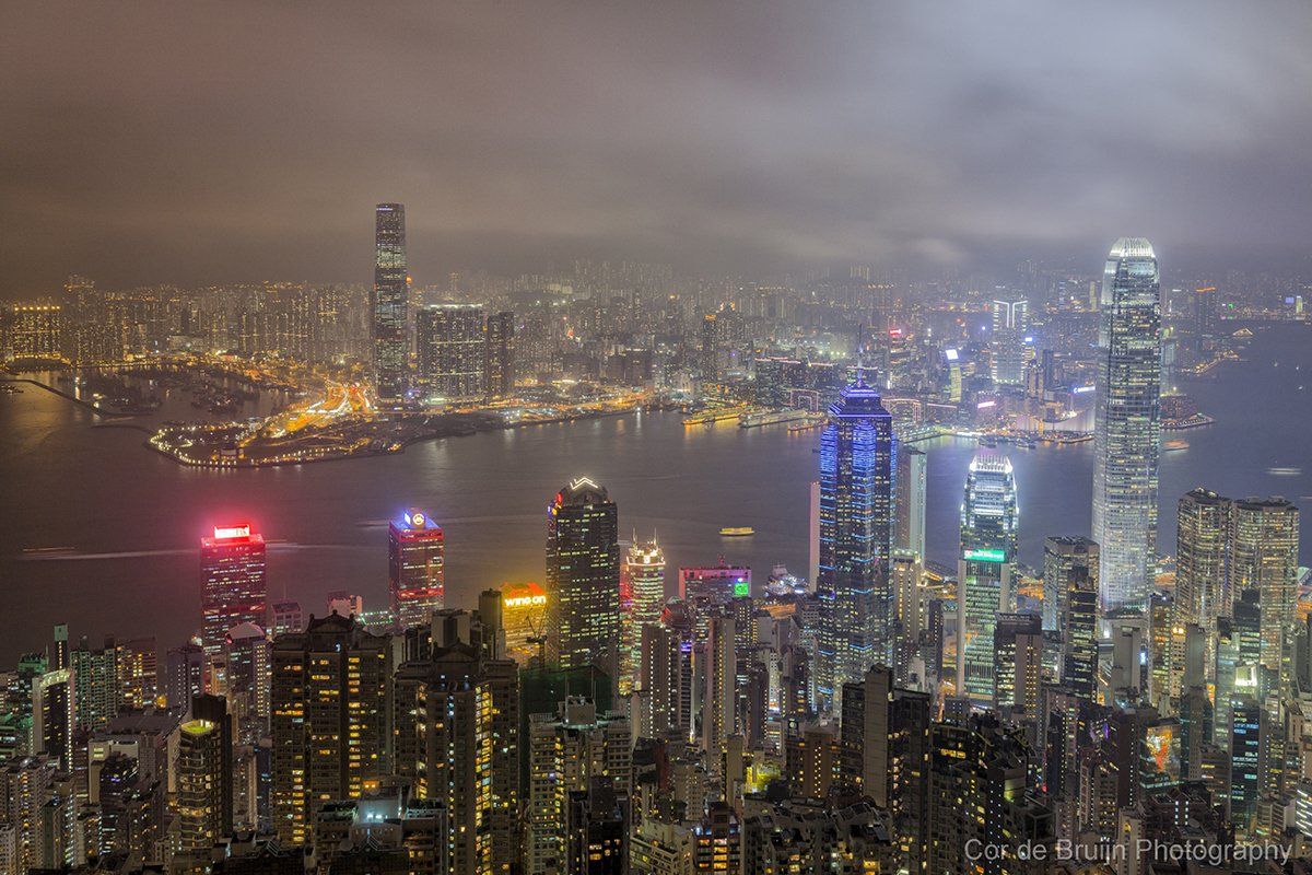 Nighttime cityscape of Hong Kong with illuminated skyscrapers and harbor.