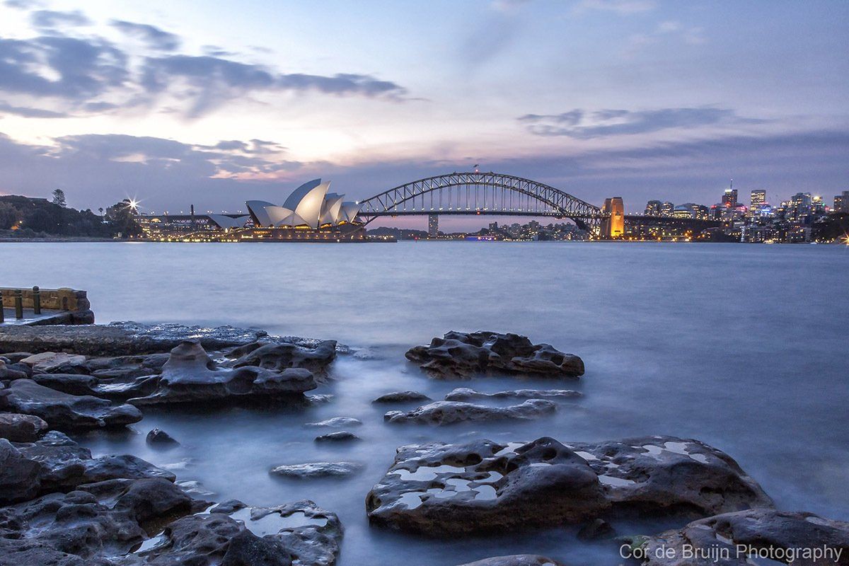 Sydney Harbour at dusk, featuring the Opera House, Harbour Bridge, and city skyline.