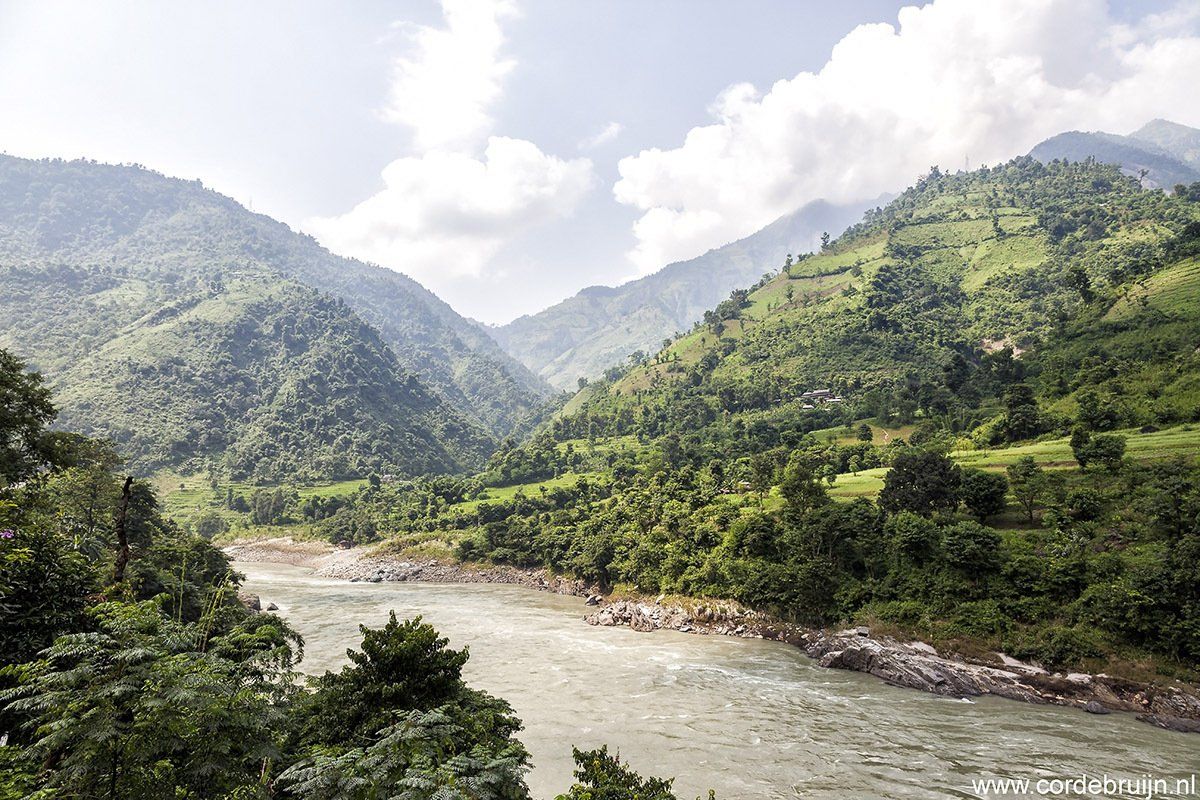 River flowing through a lush green mountain valley under a partly cloudy sky.