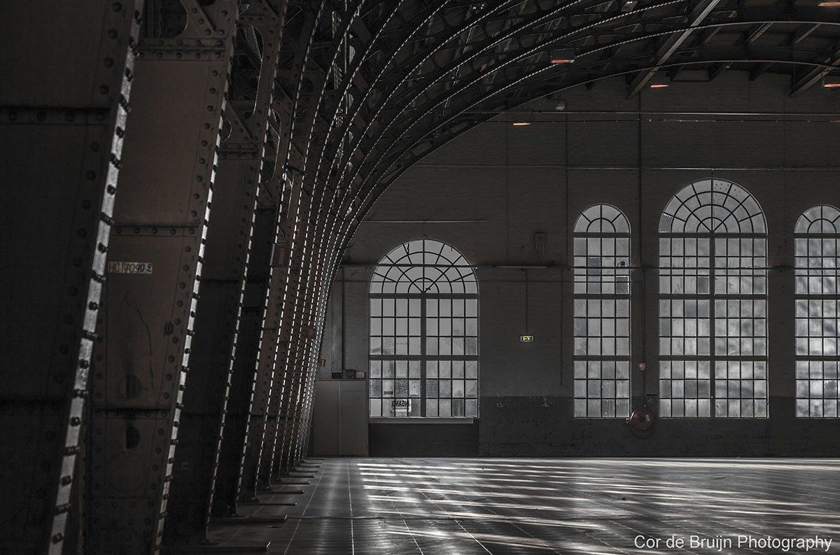 Interior of an industrial building. Arched windows with bright light illuminate the empty floor. Metal framework.