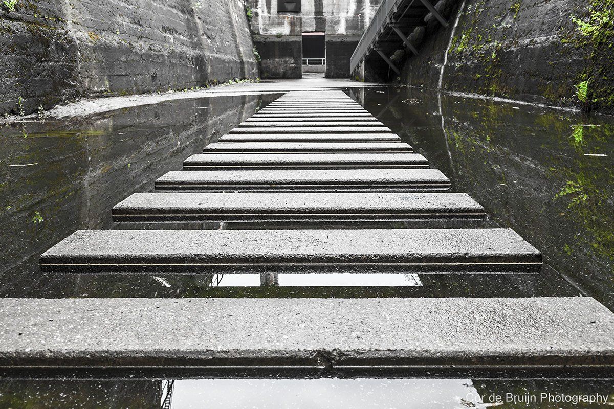 Concrete steps receding into a dark, flooded channel; overcast sky reflected in the water.