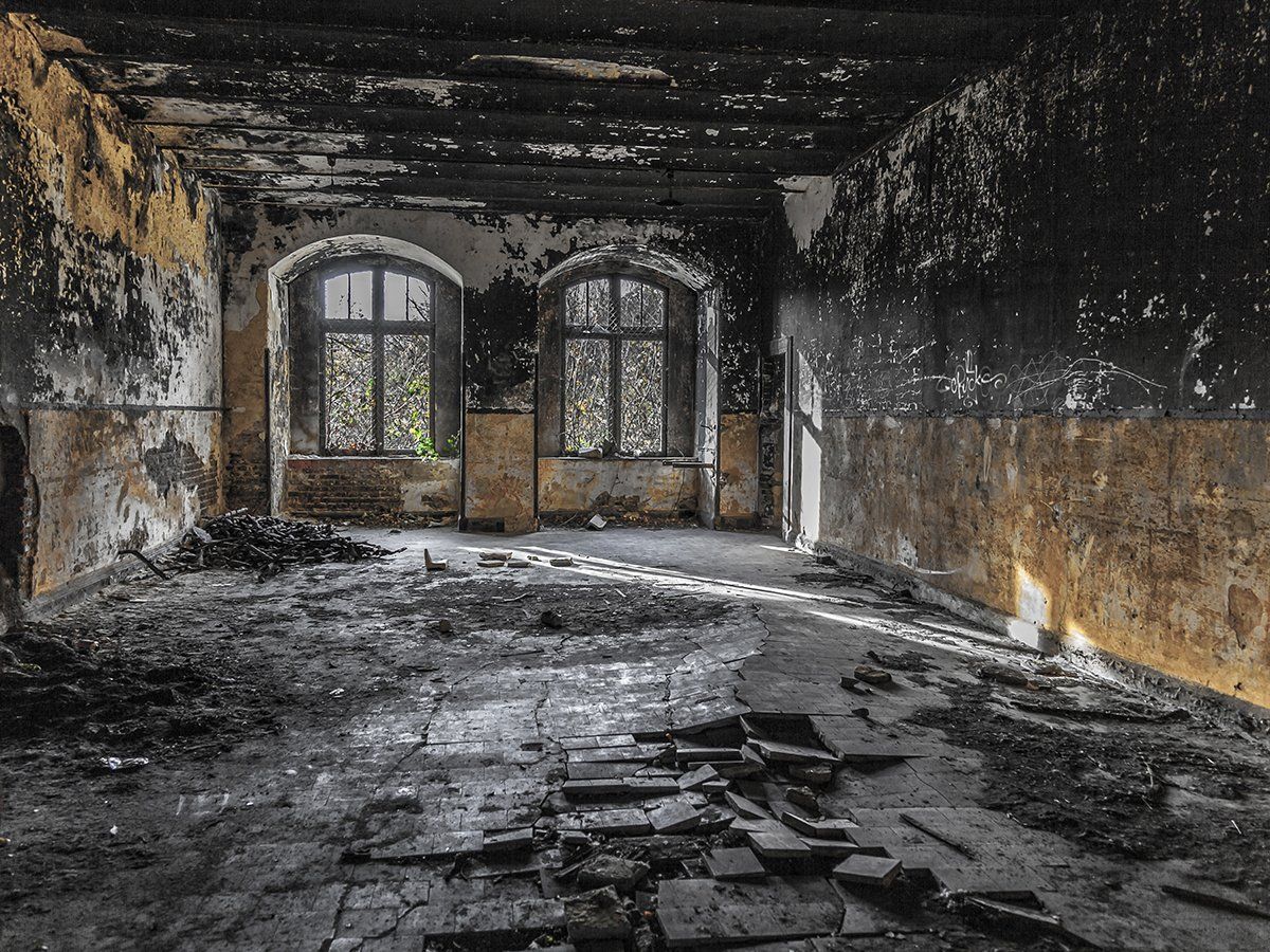 Dilapidated room with arched windows, crumbling walls, and debris on the floor; sunlight streams through windows.