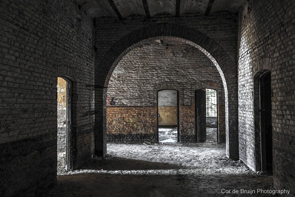 Interior of an abandoned brick building with arched doorways and peeling paint.