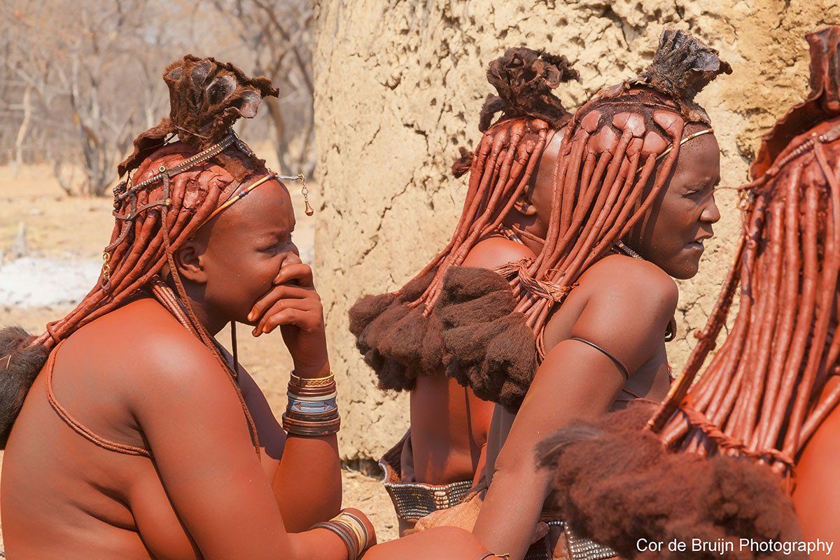 Himba women with ochre-colored skin and braided hair, adorned with jewelry.