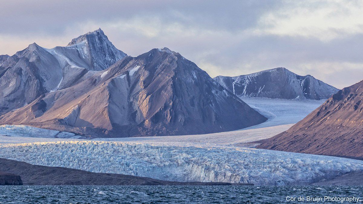 Glacier flowing between mountains, ending at a body of water. Snowy peaks, cool tones.