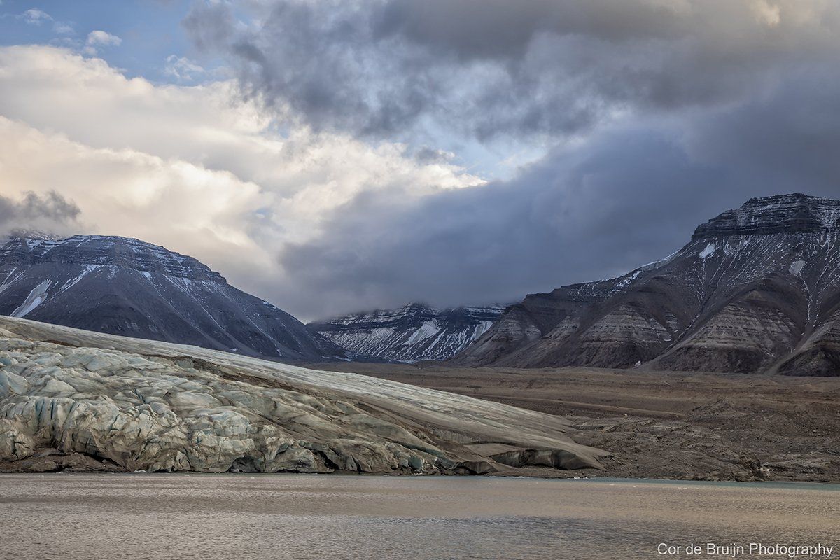 Glacier next to mountains under a cloudy sky.