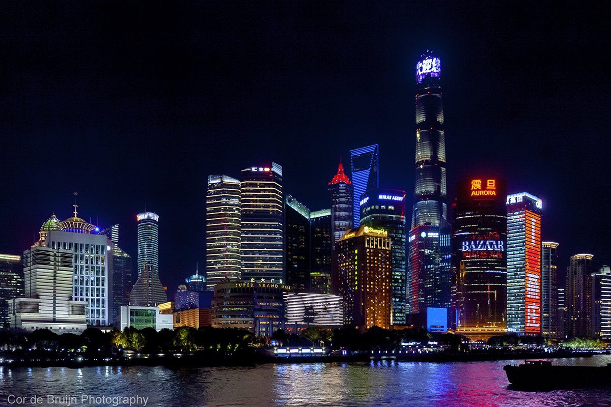 Night view of Shanghai skyline with illuminated skyscrapers reflecting on the water.