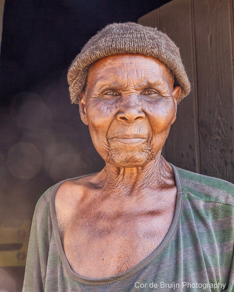Elderly person wearing a knit cap and olive-green shirt looking at the camera.