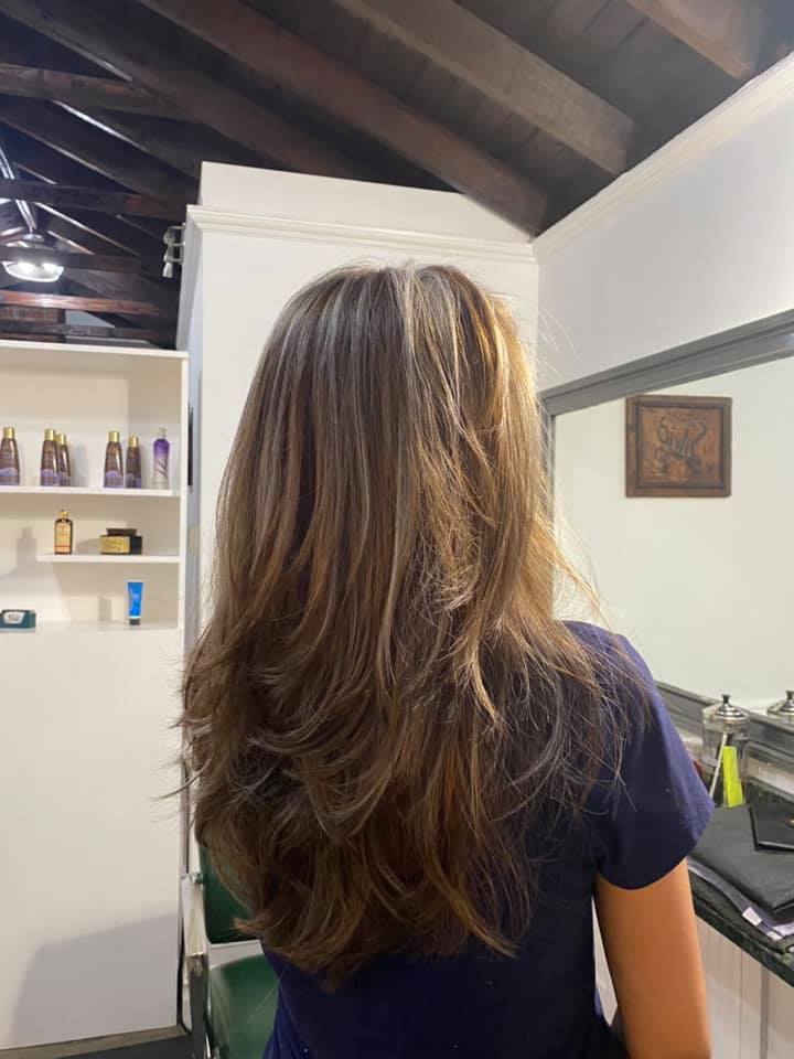 Person with long brown hair standing in a modern room, seen from behind, near shelves and a mirror.