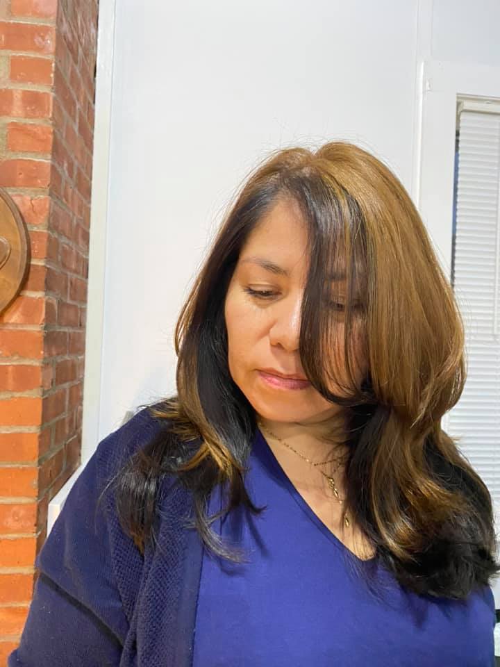 Woman in a blue top looking down, standing indoors near a brick wall and window blinds.
